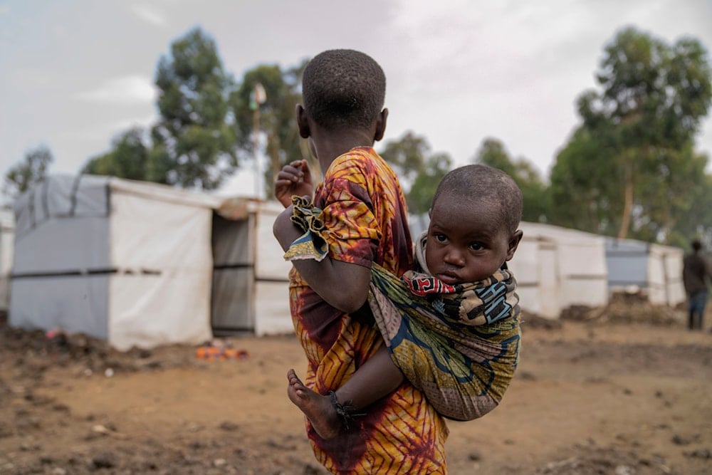 A young girl carrying her sister on her back stand outside a refugee camp on the outskirts of Goma, Democratic Republic of the Congo, Thursday, July 11, 2024. (AP)