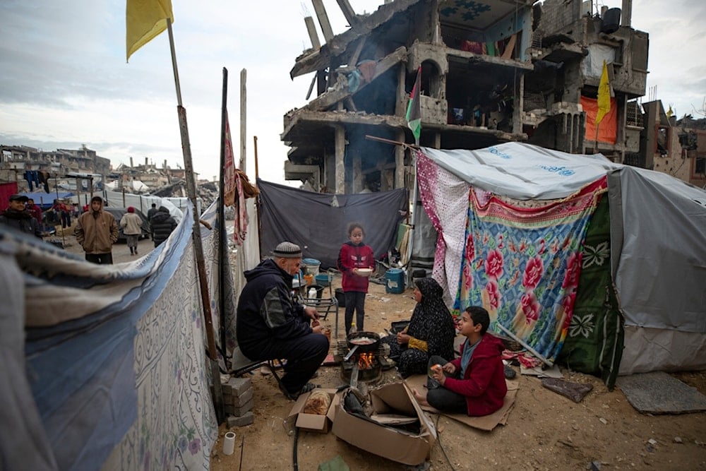 A Palestinian family cooks on fire next to their tent, in an area largely destroyed by the Israeli army's air and ground offensive in Jabaliya, Gaza Strip, on Tuesday, Feb. 11, 2025 (AP)