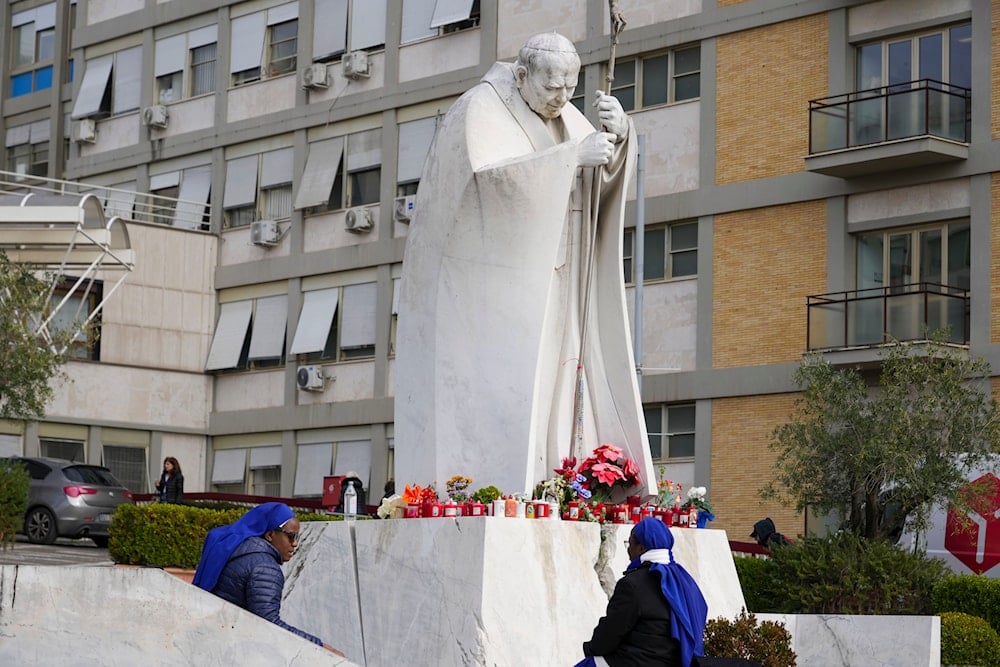 Nuns sit next to a statue of Pope John Paul II in front 