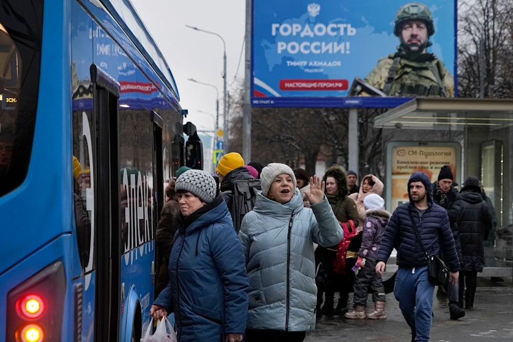 People take a bus at a bus stop with an advertising billboard displaying a Russian soldier, Timur Akhmadov, participant of the special military operation in Ukraine, with a sign reading 