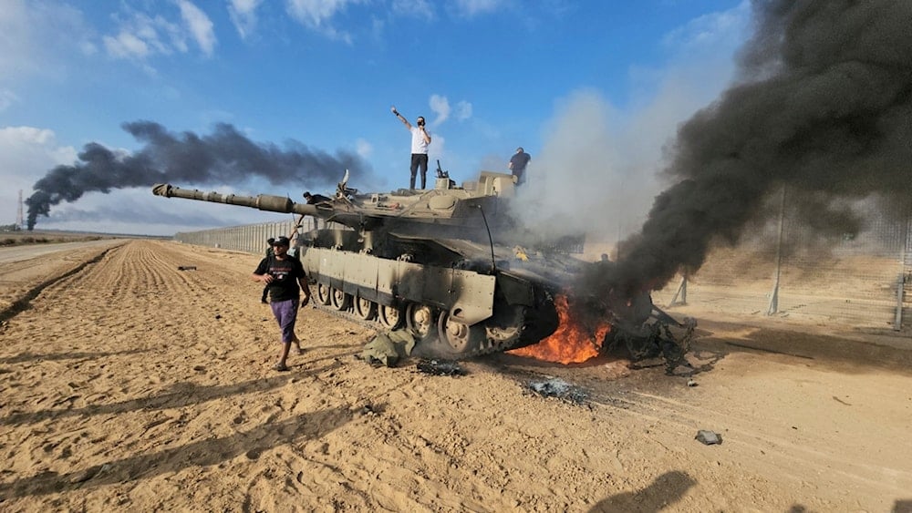 Palestinians celebrate by a destroyed Israeli tank at the Gaza Strip fence east of Khan Younis southern Saturday, Oct. 7, 2023 (AP)