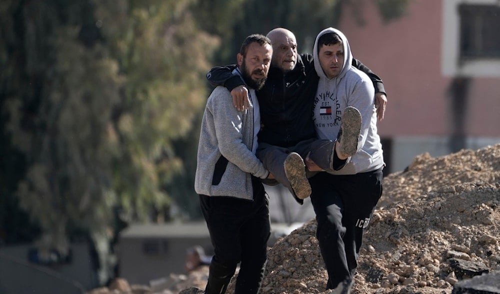 Palestinians displaced by the Israeli occupation carry an elderly man over rubble as they evacuate the Jenin refugee camp in the West Bank on Thursday, Jan. 23, 2025. (AP)