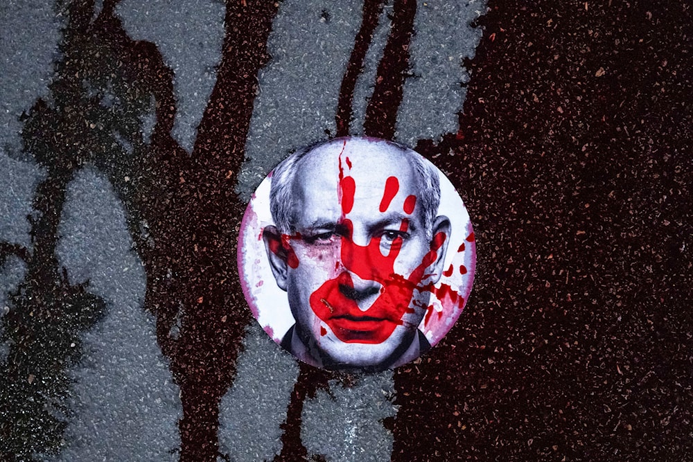 Israeli protesters stuck a sticker with the face of Israeli Prime Minister Benjamin Netanyahu on a road and poured red liquid, symbolizing blood, over it, in occupied al-Quds, Feb. 17, 2025. (AP)