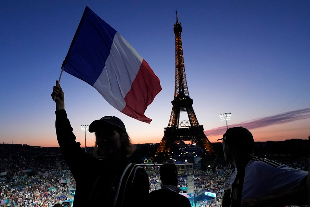 A spectator waves a French flag before a beach volleyball match between the US and Czechia at the 2024 Summer Olympics, Sunday, July 28, 2024, in Paris, France. (AP Photo/Robert F. Bukaty)