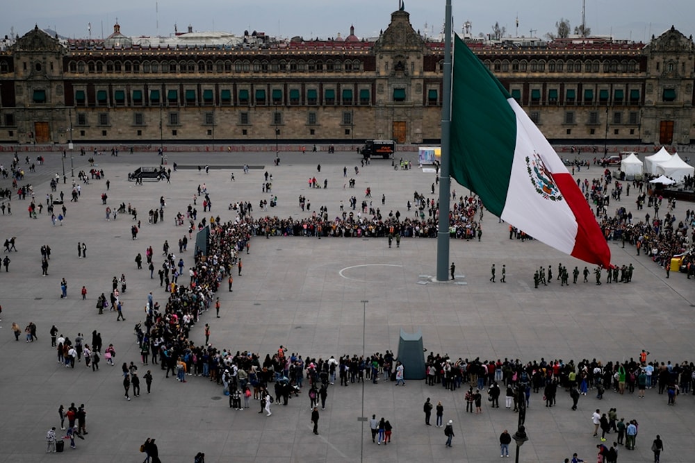 People watch the lowering of the flag ceremony at the Zocalo in Mexico City, Saturday, Jan. 20, 2024 (AP Photo/Natacha Pisarenko)