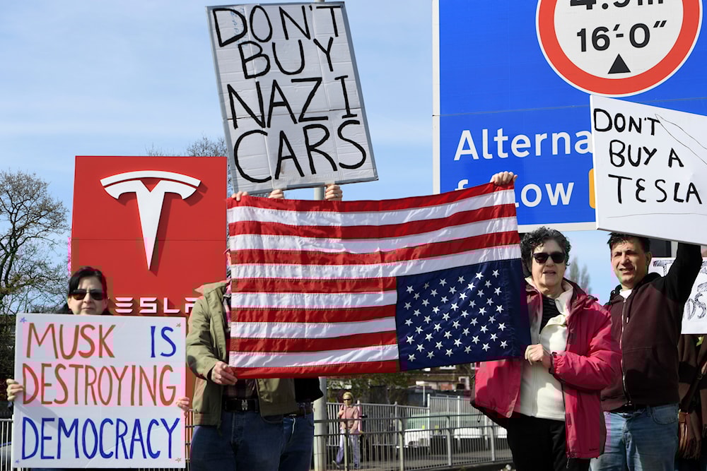 Protesters hold placards as they take part in the Tesla Takedown Global Day of Action near a Tesla dealership in London, Saturday, March 29, 2025 (AP)