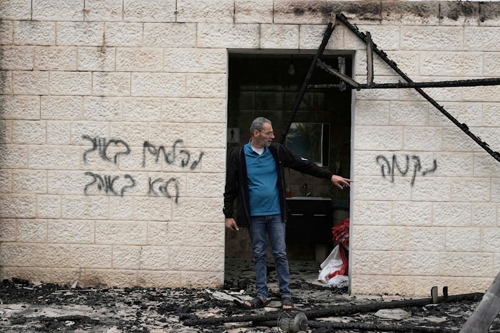 Mustafa Salama stands in the ruins of a wedding hall torched in an apparent settler attack in the West Bank town of Biddya, Tuesday, April 8, 2025. Hebrew graffiti: 