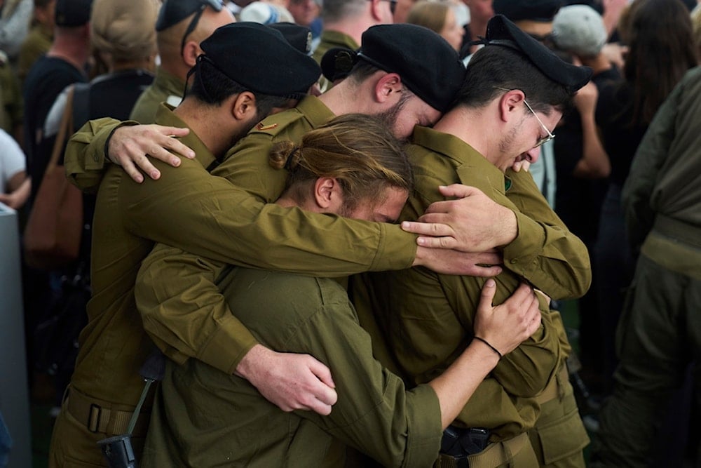 Israeli soldiers stand in a group hug mourn another who was killed in a ground operation in the Gaza Strip, during his funeral service in the Gezer regional council in occupied Palestine, April 27, 2025 (AP)