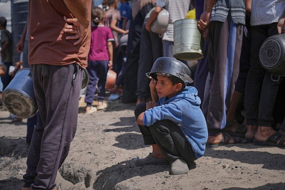 A boy holds an empty pot over his head as he waits for donated food at a community kitchen in Khan Younis, in the southern Gaza Strip, Friday, May 9, 2025 (AP)