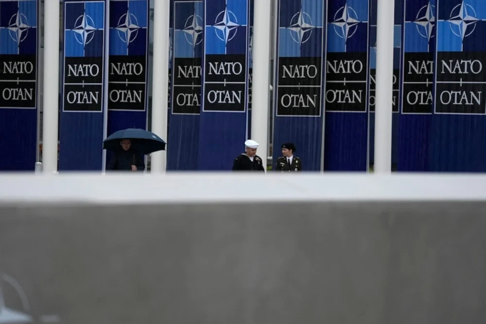 Two military personnel walk by NATO banners prior to a wreath-laying ceremony at NATO headquarters in Brussels, April 4, 2024 (AP)