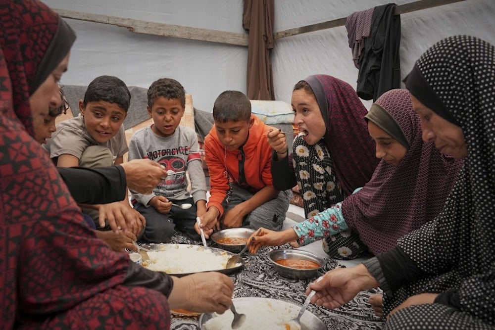 The Al-Najjar family eats peas with rice in their family tent in Muwasi, on the outskirts of Khan Yunis in the southern Gaza strip, April 25, 2025 (AP/Abdel Kareem Hana)