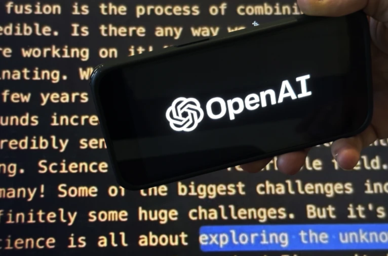 The OpenAI logo appears on a mobile phone in front of a screen showing part of the company website in this photo taken on November 21, 2023 in New York (AP/Peter Morgan)