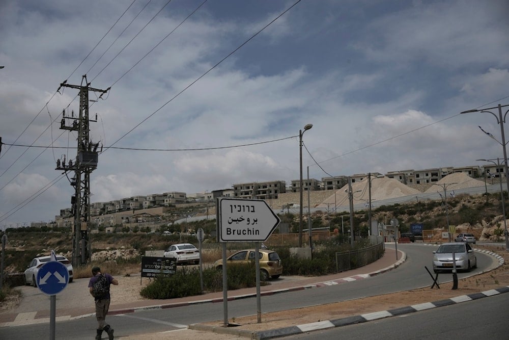An Israeli settler walks to a bus stop outside of the West Bank settlement of Bruchin, occupied Palestine, Thursday, May 15, 2025 (AP)
