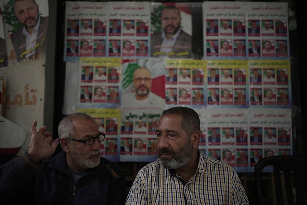 A voter, left, shows his ink-stained finger as he speaks with a friend in front of campaign posters for municipal election candidates in the southern suburbs of Beirut, Lebanon, Sunday, May 4, 2025 (AP)