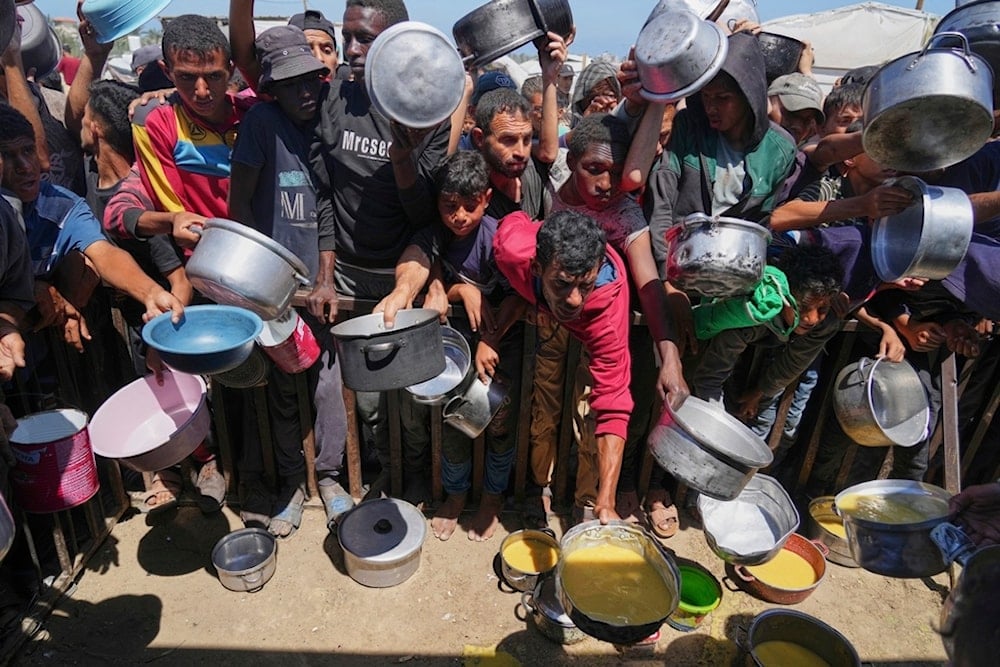 Palestinians struggle to receive cooked food distributed at a community kitchen in the Muwasi area of Khan Younis, in the Gaza Strip, Friday, May 23, 2025. (AP Photo/Abdel Kareem Hana)