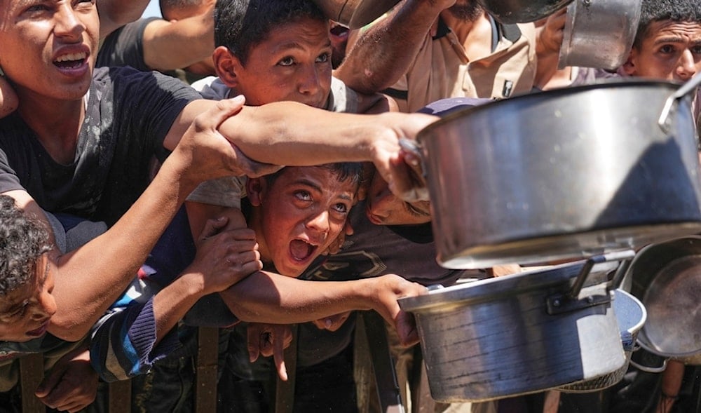 Palestinians struggle to receive cooked food distributed at a community kitchen in the Muwasi area of Khan Younis, in the Gaza Strip, Friday, May 23, 2025. (AP)