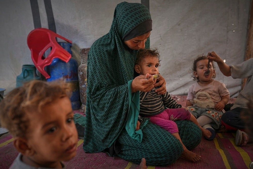 A Palestinian woman feeds her children at a tent sheltering a displaced family in central Gaza City, Saturday, May 24, 2025 (AP)