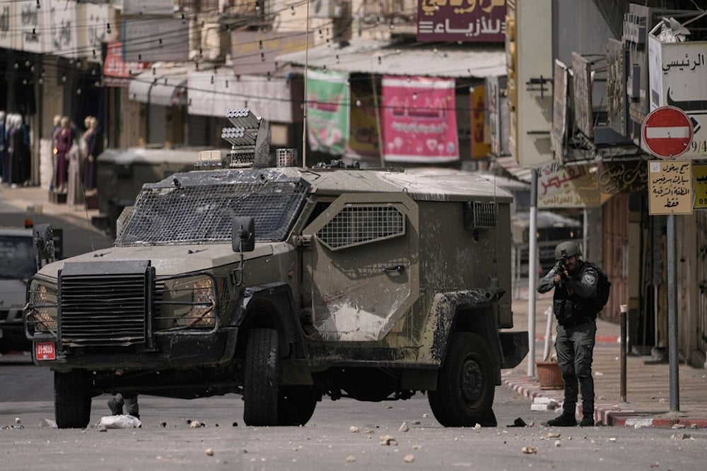An Israeli soldier aims his weapon as he stand next to an armoured vehicle during a military raid in the West Bank city of Nablus, Tuesday, May 27, 2025. (AP Photo/Majdi Mohammed)