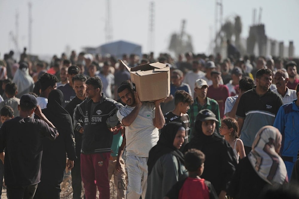 Palestinians carry boxes containing food and humanitarian aid packages delivered by the Gaza Humanitarian Foundation, a US-backed organization approved by the Israeli occupation in Rafah, southern Gaza Strip, on Tuesday, May 27, 2025 (AP)