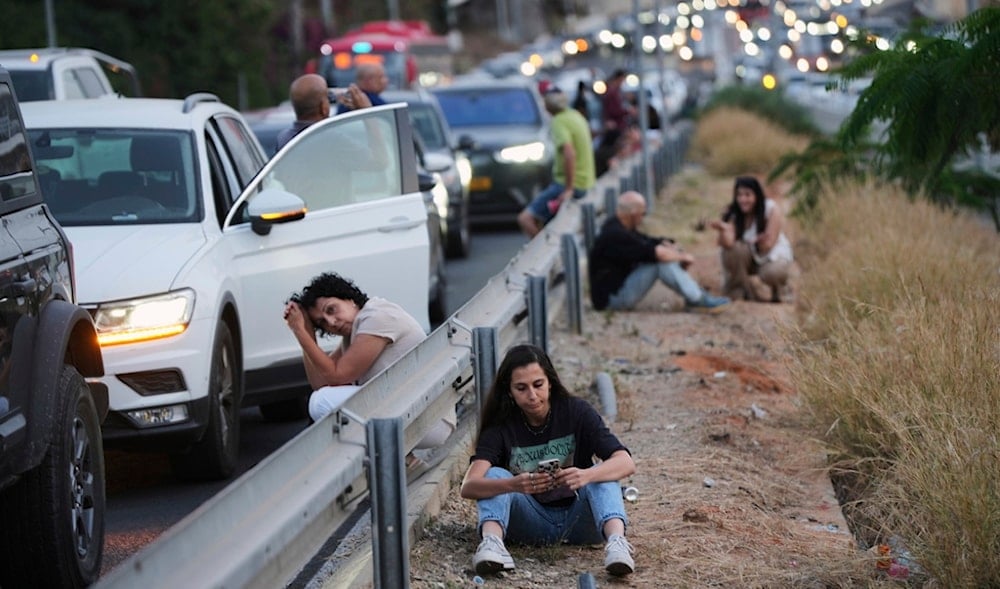 Settlers take cover on the side of a highway as a siren sounds a warning following a missile that was launched from Yemen, in occupied Palestine, Tuesday, May 13, 2025. (AP)