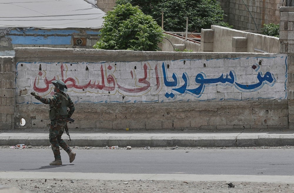 A Syrian government security forces gunman passes in front of an Arabic graffiti that reads 