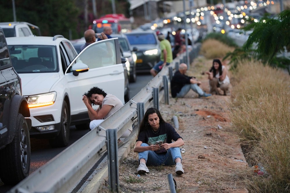 People take cover on the side of a highway as a siren sounds a warning following a missile that was launched from Yemen, in Tel Aviv, occupied Palestine on May 13, 2025. (AP Photo/Ohad Zwigenberg)