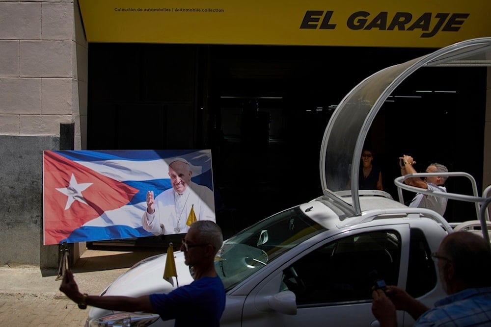 People take photos by a photo of Pope Francis at the entrance to the car museum exhibiting one of the Popemobiles he used during his visit to Cuba in Havana, Tuesday, April 22, 2025. (AP)