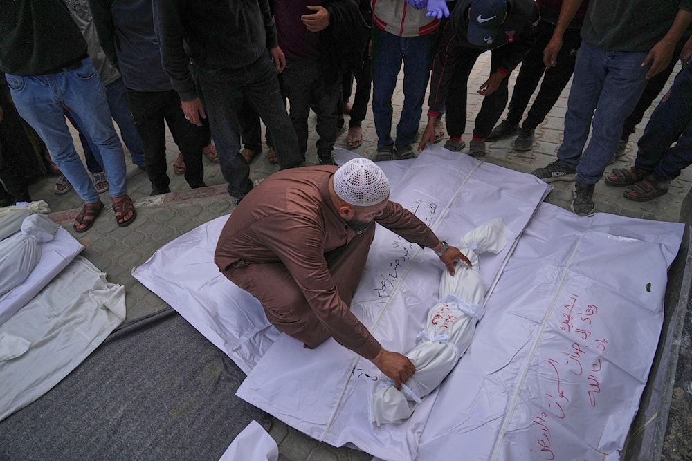 A morgue worker places the body of a child among the bodies of other victims killed in at least two separate Israeli army strikes, ahead of a burial ceremony outside Al-Shifa hospital in Gaza City, Monday, May 5, 2025. (AP Photo/Jehad Alshrafi)