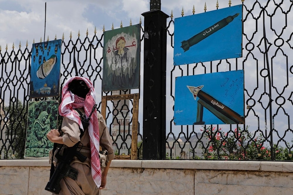 A Yemeni gunman walks past paintings depicting rockets and scenes in solidarity with Gaza, displayed on a roadside fence in Sanaa, Yemen, Monday, May 5, 2025 (AP)