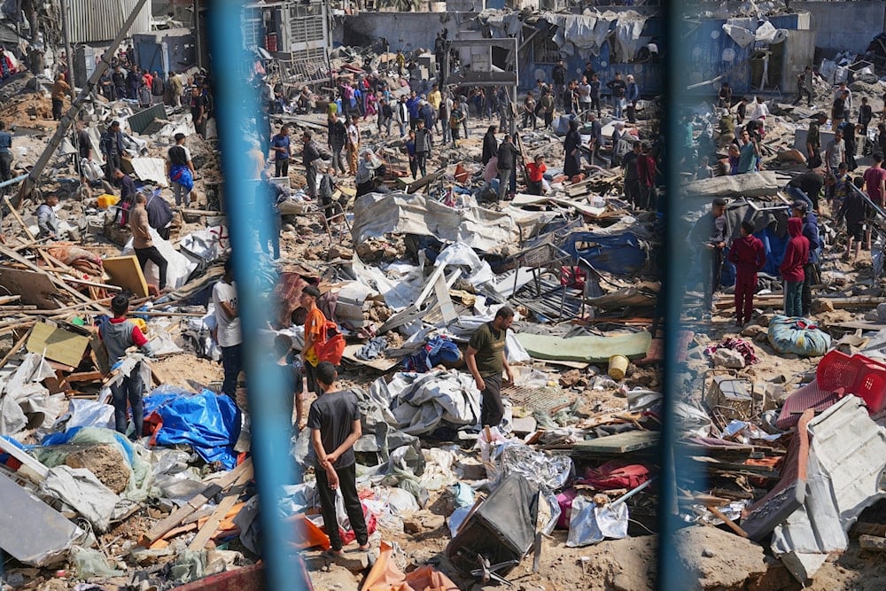 Palestinians collect belongings from a school used as a shelter by displaced residents that was hit twice by Israeli army strikes on Tuesday, killing more than 25 people, in Bureij, central Gaza Strip, Wednesday, May 7, 2025 (AP)