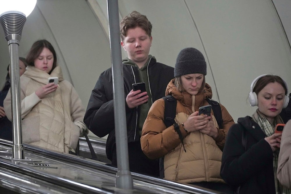 People check their smartphones as they go down a subway escalator in St. Petersburg, Russia, Tuesday, March 18, 2025. (AP Photo/Dmitri Lovetsky)