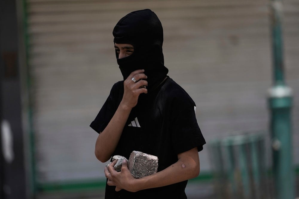 A masked Palestinian demonstrator holds rocks during confrontations with Israeli forces following a military raid in the West Bank city of Nablus, Tuesday, June 10, 2025 (AP)