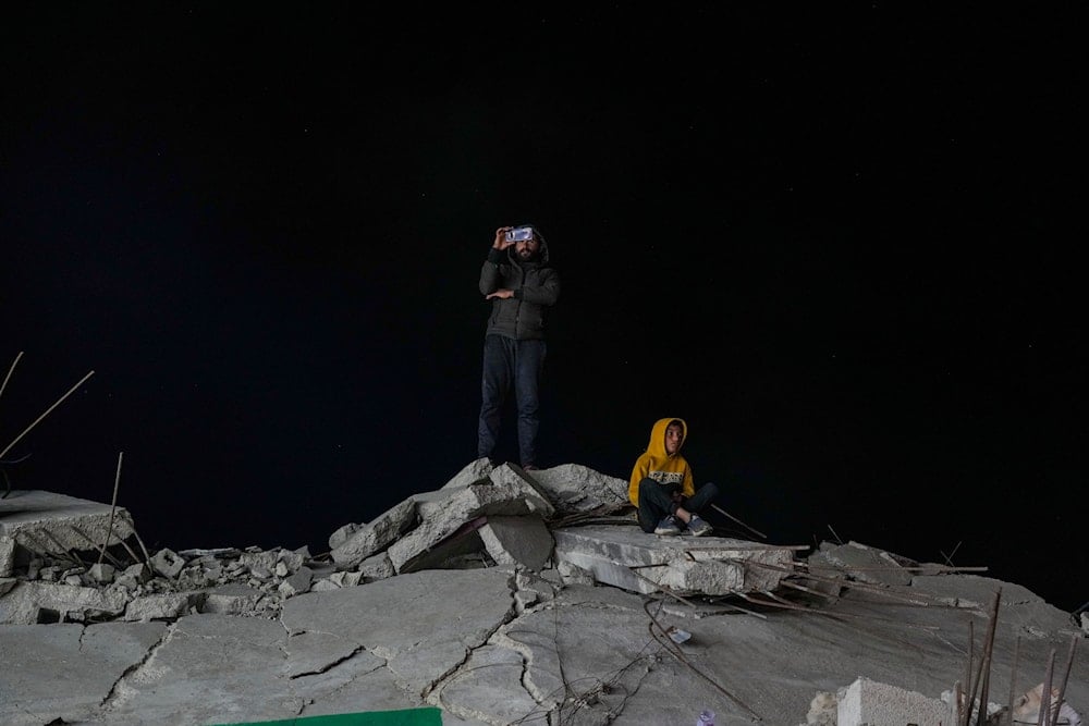 A Palestinian boy sits on the rubble of a building destroyed by Israeli airstrikes while a man takes pictures with his cellphone, in Rafah, southern Gaza Strip, on  Saturday, March 1, 2025. (AP)