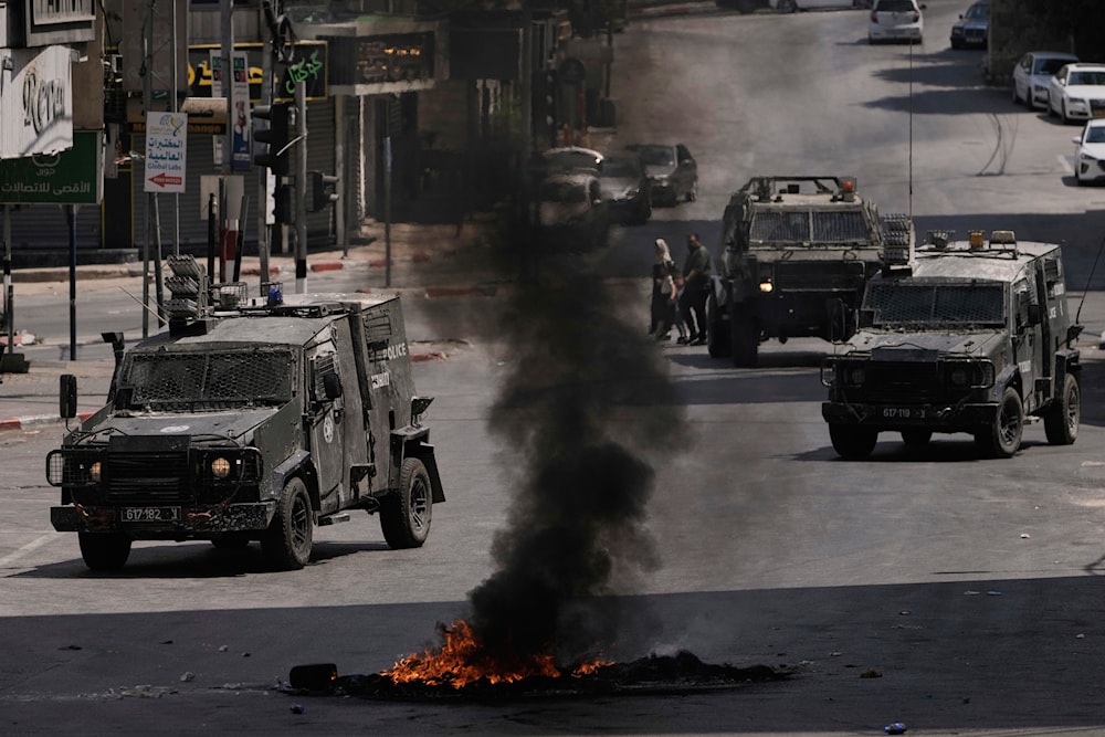 Israeli armoured vehicles drive past burning tires during a military raid in the West Bank city of Nablus, Tuesday, June 10, 2025 (AP)