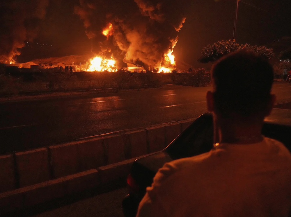 A man looks at flames rising from an oil storage facility after it was struck by an Israeli strike in Tehran, Iran on June 15, 2025. (AP)