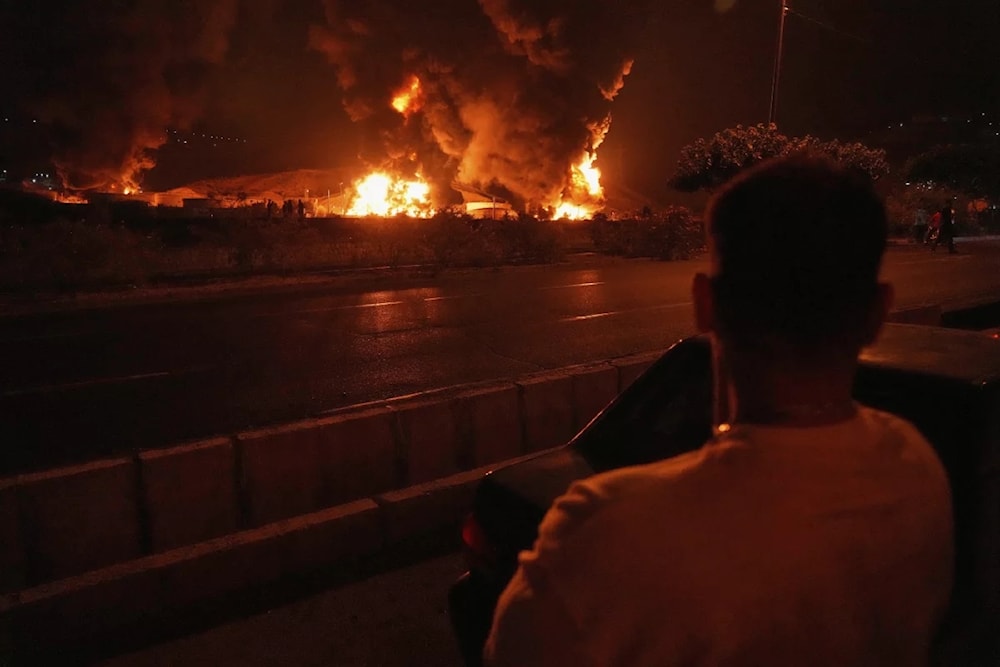 A man looks at flames rising from an oil storage facility after it appeared to have been struck by an Israeli strike in Tehran, Iran, early Sunday June 17, 2025 (Vahid Salemi/AP)