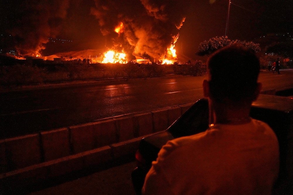 A man looks at flames rising from an oil storage facility after it was struck by an Israeli strike in Tehran, Iran, early Sunday, June 15, 2025 (AP)