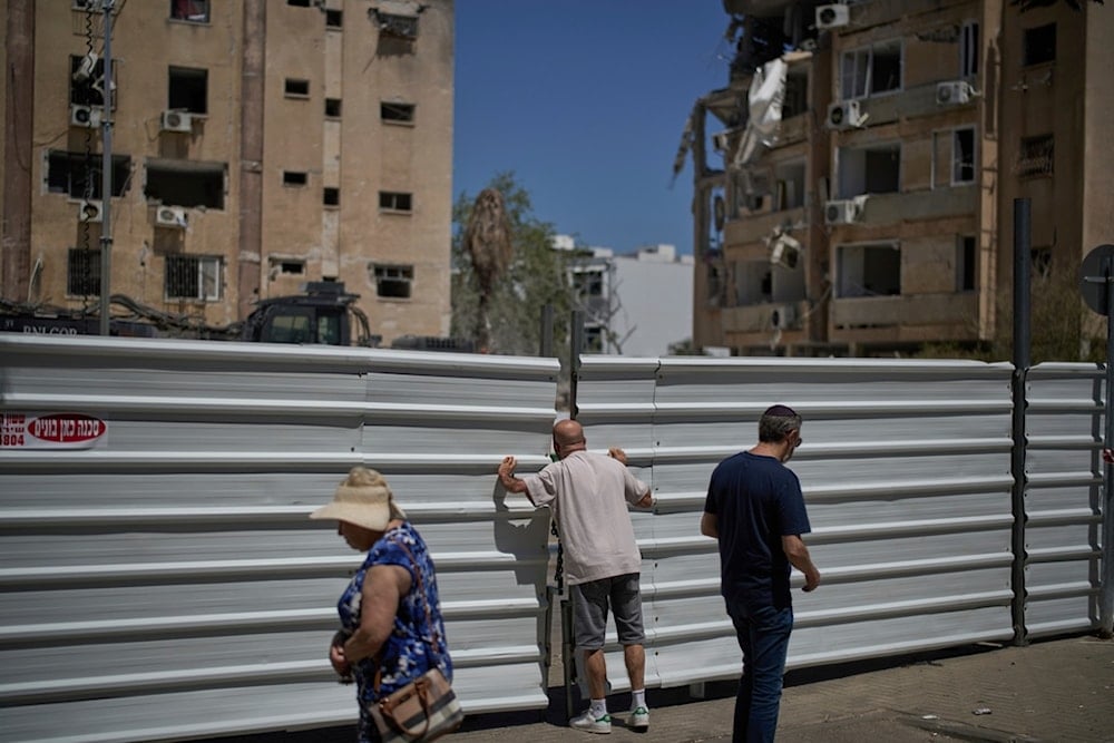 A man peeks from a fence a day after of an Iranian missile hit a residential area in Holon, near Tel Aviv, occupied Palestine, Friday, June 20, 2025. (AP Photo/Leo Correa)