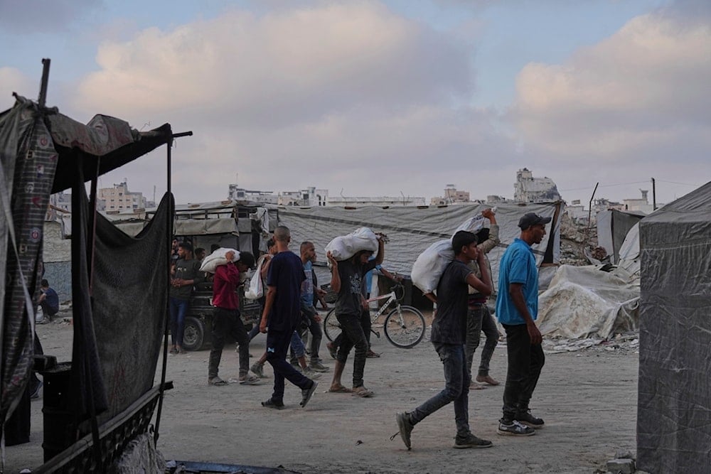 Palestinians carry sacks of food and humanitarian aid unloaded from a truck convoy that had been heading to Gaza City, in the northern Gaza Strip, Sunday, June 22, 2025 (AP)