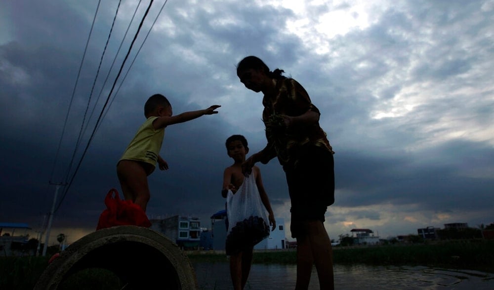 A woman is silhouetted as she collects river shells with her grand children at a flooded land following recent rain on the outskirts of Phnom Penh, Cambodia, Thursday, June 11, 2020. (AP)