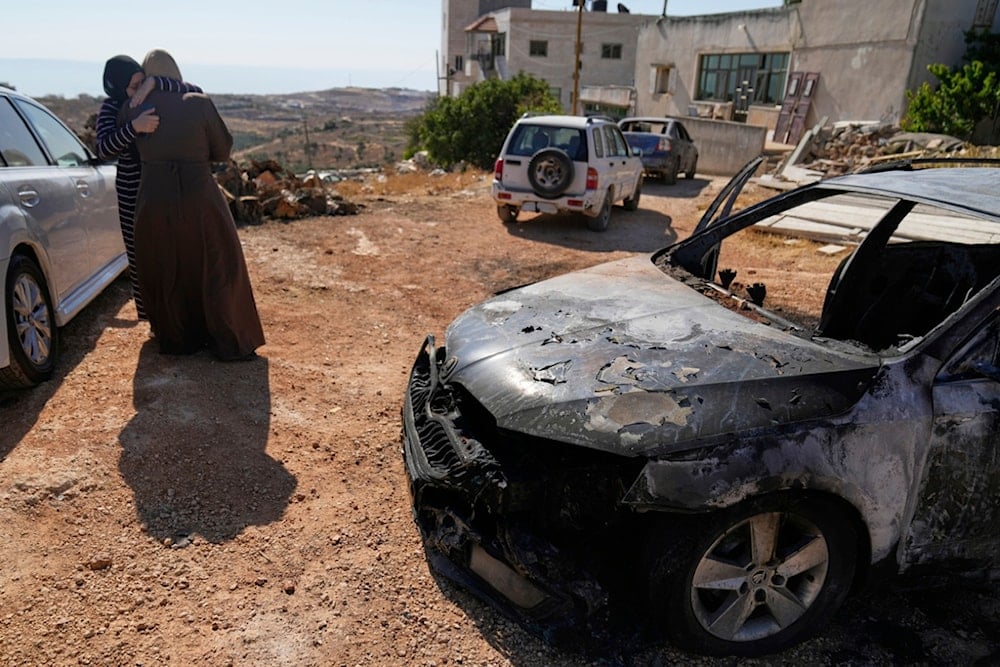 Women comfort each other by a vehicle that was burnt overnight by Israeli settlers in an attack that killed three Palestinians and burnt several vehicles and damaged homes, in Kafr Malik, east of Ramallah, Thursday, June 26, 2025 (AP)