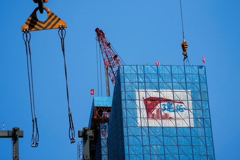 A crane cables swing by a construction site displaying an advertising banner showing a Communist Party flag, in the Central Business District in Beijing on Wednesday, May 8, 2024. 
