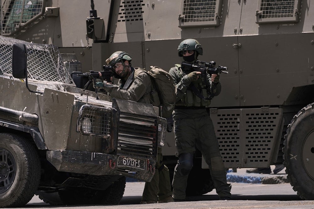 An Israeli soldier aims his weapon next to armoured vehicles during a military raid in the West Bank city of Nablus, on May 27, 2025. (AP Photo/Majdi Mohammed)