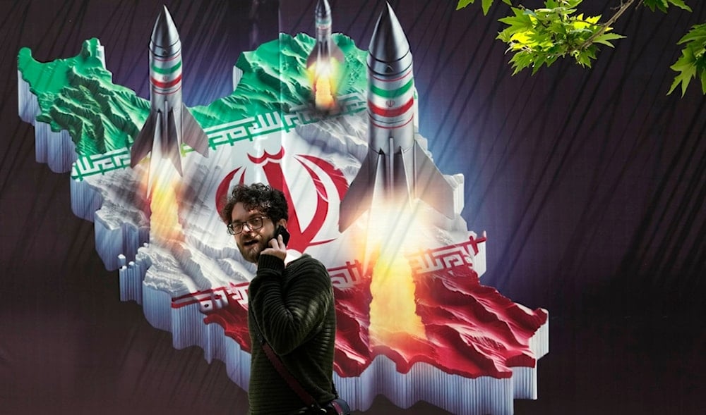 A passerby, taking on his cellphone, walks past a banner showing missiles being launched from Iranian map in northern Tehran, Iran, Friday, April 19, 2024. (AP)