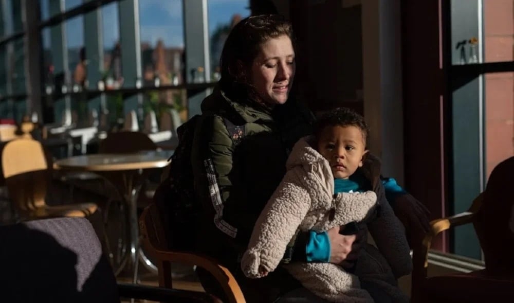 A customer of thje Coventry Foodbank centre in Queens Road BAptist Church sits with her one-year-old son before collecting her food parcel in Coventry, UK, undated (AFP)