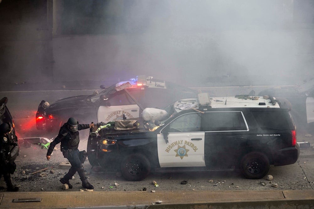 A California Highway Patrol officer pulls an electric scooter off a vehicle on a highway as protesters throw objects at the police vehicles near the Metropolitan Detention Center in downtown Los Angeles, Sunday, June 8, 2025 (AP)