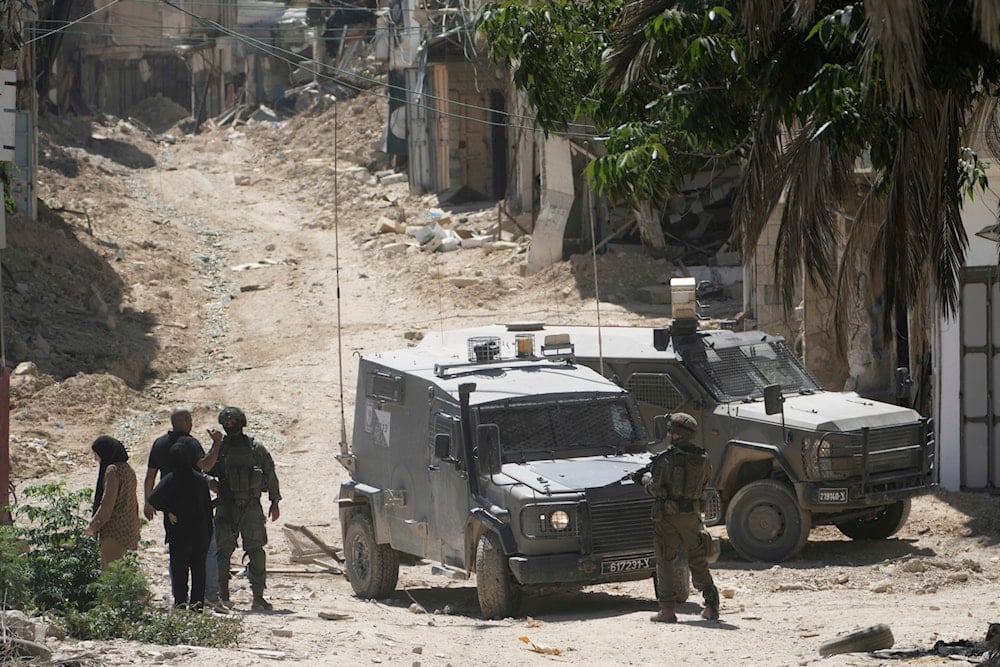 Israeli soldiers speak with Palestinians in the West Bank urban refugee camp of Tulkarm, Occupied Palestine, Sunday, July 6, 2025 (AP)