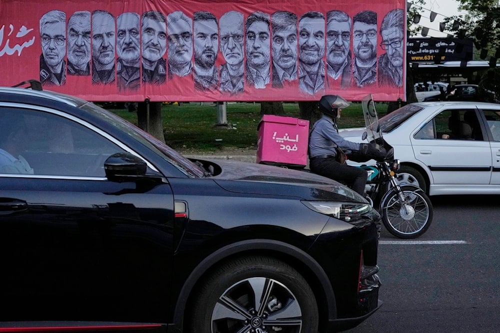 Vehicles drive past a banner showing portraits of the Iranian armed forces commanders and nuclear scientists who were killed in an Israeli strike, at Tajrish Square in northern Tehran, Iran, Monday, June 30, 2025 (AP)