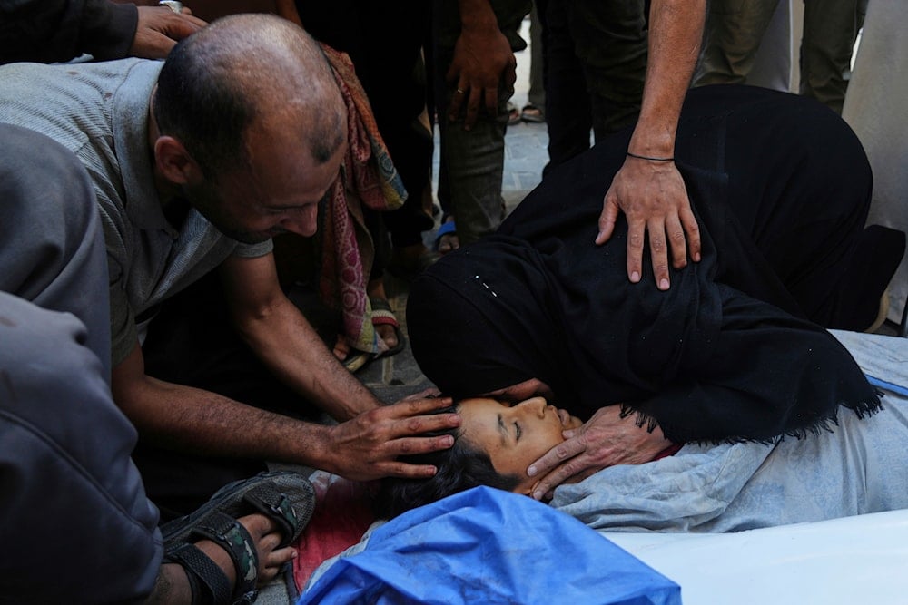 Relatives mourn over the body of 13-year-old Seraje Ebrahim, who was killed in an Israeli strike that targeted a drinking water distribution point, at Al-Awda Hospital in Nuseirat, central Gaza Strip, Sunday, July 13, 2025. (AP Photo/Abdel Kareem Hana)