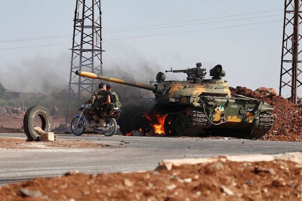 Syrian government soldiers on a motorcycle pass by a burning tank on the outskirts of Sweida city, where clashes erupted between the Druze community and Bedouine clans, in southern Syria, Monday, July 14, 2025 (AP)